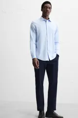 Camisa celeste a rayas verticales blancas, de corte recto, con cuello italiano abierto, manga larga con puños abotonados y cierre frontal con botones.