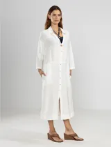 Camisa larga blanca de lino italiano, con cuello clásico, mangas 3/4, silueta fluida, dobladillo curvado en las costuras laterales y bolsillos discretos.