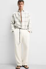 Pantalón color crema de lino, corte amplio, con pliegues frontales, bolsillos laterales y traseros de ojal. Cierre frontal con cremallera y gancho metálico oculto.