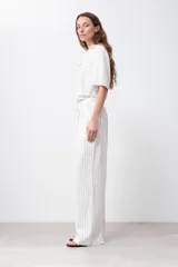 Pantalón de lino color blanco con finas rayas verticales negras, corte palazzo, cintura alta con pinzas y cinturón marrón.