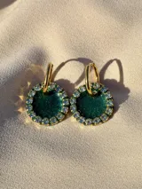 Par de aros colgantes con forma circular, de resina color verde esmeralda con glitter y borde de strass. Cierre con aro de acero quirúrgico dorado.
