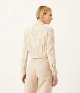Camisa de crepé color beige con estampado geométrico en tonos neutros, cuello camisero, manga larga y cierre con botones. Tiene un lazo frontal para atar.