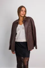 Camisa oversize de cuerina color marrón, con cuello clásico, cierre frontal con botones y bolsillo de parche en el pecho.