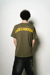 Remera verde oliva de corte regular fit, confeccionada en jersey de algodón. Presenta un pequeño logo bordado en el pecho y un estampado grande con el nombre de la marca en la espalda, ambos en color amarillo.