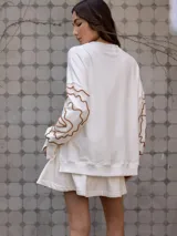 Buzo blanco de jogging sin friza, con cuello redondo y bordado floral marrón en las mangas.