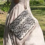 Sobre de cuero vacuno con estampado reptil, forrado y con bolsillo interior. Incluye correa de cadena desmontable y agarradera manual de cuero.