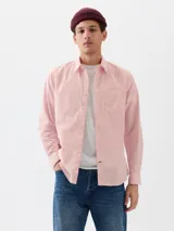Camisa de manga larga color rosa claro, con cuello clásico, botones frontales y un bolsillo de parche en el pecho izquierdo.