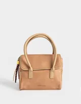 Cartera tipo city color beige, de tela deportiva, con doble asa corta, correa regulable desmontable, solapa con broche a presión y charm colgante.