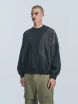 Buzo de cuello redondo, color negro, confeccionado en frisa gamuzada de algodón con recortes en microfibra, creando un efecto de capas. Presenta un bolsillo frontal tipo parche con cierre a presión.