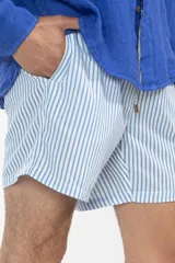 Short de baño celeste con rayas verticales blancas, cintura elástica con cordón ajustable, bolsillos laterales y trasero con cierre, logo de la marca bordado en la pierna.