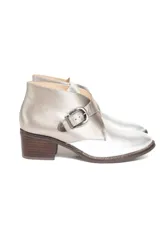 Botín plateado de cuero con efecto metalizado, corte lateral en forma de V y ajuste con hebilla. Tiene taco de madera bajo.