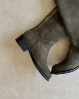 Bota alta de cuero color verde musgo, con caña recta, taco bajo y cierre lateral. Incluye funda de cuero con cierre.