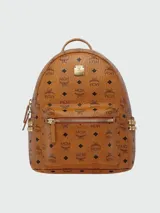 Mochila MCM de lona revestida con estampado del logo de la marca en color marrón. Cuenta con tachuelas doradas, cierre de cremallera, bolsillo frontal con cremallera y asa superior.