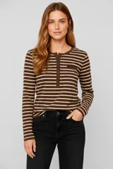 Remera de manga larga con cuello redondo y abertura frontal con botones. Presenta un patrón de rayas horizontales blancas y negras, y un pequeño bolsillo negro en el pecho.