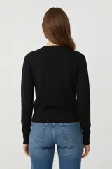 Cardigan de tejido de punto, color negro con rayas horizontales blancas, corte al cuerpo y cuello redondo a la base. Posee cierre frontal con botones dorados.