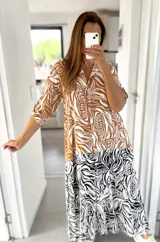 Vestido largo tipo camisero con estampado abstracto en tonos marrón, blanco y negro. Tiene cuello camisero, mangas 3/4 y cierre frontal con botones.