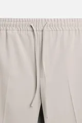 Pantalón color arena de corte recto, confeccionado en tejido elástico. Cuenta con cintura elástica ajustable con cordón, bolsillos laterales y bolsillos de vivo en la parte trasera.