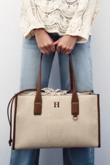 Bolso maxi shopper de hombro color beige con detalles en cuero marrón. Tiene doble asa de cuero y bolsa de tela extraíble con cierre fruncido.