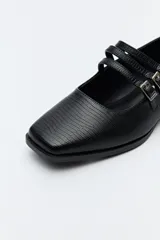 Zapato tipo Mary Jane color negro con textura de reptil, de charol sintético con punta cuadrada y triple tira con hebillas.