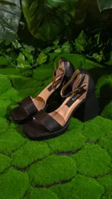 Sandalias negras de cuero sintético, con plataforma y taco cuadrado. Tiras anchas sobre el empeine y pulsera al tobillo con hebilla metálica.