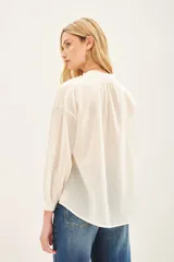 Camisa blanca de voilé de algodón con escote redondo y bordados de ojos en el delantero. De corte recto y mangas largas con puños abotonados.