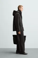 Parka negra de tejido técnico acolchado, corte regular fit, cuello alto con capucha ajustable, manga larga con puños ajustables, bolsillos de solapa en la cadera y bolsillo interior. Cierre frontal con cremallera oculta y botones a presión.