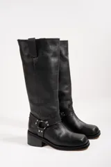 Bota de caña alta color negro, confeccionada en cuero. Presenta una correa con hebilla y argolla metálica alrededor del tobillo.