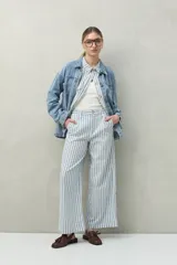 Pantalón de lino a rayas verticales azules y blancas, de corte amplio y relajado, con bolsillos laterales y cierre frontal con botón.