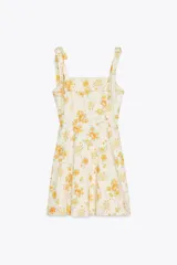 Vestido corto de popelina color crema con estampado de rosas amarillas, escote recto y tirantes con lazos. Tiene forro interior y cierre trasero con cremallera oculta.