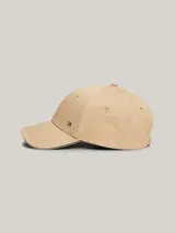 Gorra de béisbol clásica de seis paneles color beige, confeccionada en algodón. Presenta un pequeño logo rectangular de Tommy Hilfiger en la parte delantera y ribetes con los colores distintivos de la marca en el borde de la visera.