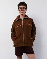 Chaqueta marrón de pana con forro polar, cierre frontal con cremallera y bolsillos laterales. Presenta bordados a mano en forma de zigzag en el frente y los bolsillos.