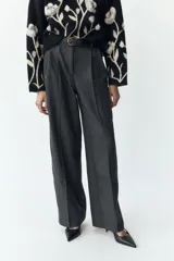 Pantalón negro de tiro alto con pinzas delanteras, pernera ancha y cinturón de cuero con hebilla dorada.