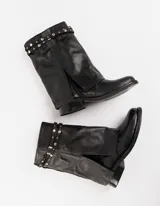 Bota corta de cuero color marrón con suela de goma negra, taco de madera de 3cm y caña de 25cm. Presenta una correa con hebilla y tachas pequeñas alrededor del tobillo.