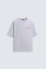 Sudadera lila de corte holgado con cuello redondo y manga corta. Presenta textos estampados en color rojo en el frente y la espalda. Tiene efecto lavado y acabados irregulares.