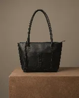 Cartera tote de cuero vacuno color negro, con forrería y cierre. Presenta un bolsillo externo con detalle de costuras y flecos.