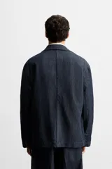 Blazer azul oscuro de denim, corte relaxed fit, con cuello de solapas de muesca, manga larga con puños abotonados, bolsillos de solapa en la cadera, abertura en el centro de la espalda y cierre frontal con botones. Sin forro interior.