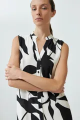 Vestido corto sin mangas, con cuello en V y estampado abstracto en blanco y negro. Tiene cierre frontal con botones y volado en el ruedo.