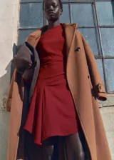 Vestido corto color borgoña, con escote asimétrico, manga larga con puños fruncidos y falda con bajo asimétrico y drapeado en la cintura. Cierre lateral con cremallera.