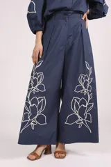 Pantalón palazzo azul marino con bordado de flores blancas en la parte inferior de ambas piernas. El pantalón tiene talle alto y pinzas en la cintura.