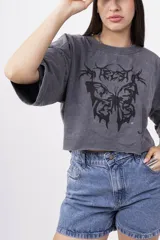 Remera gris oscuro con efecto lavado, corte crop y estampado frontal de mariposa con detalles tribales en negro.