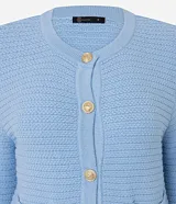 Cardigan de punto blanco, con cuello redondo, manga larga y cierre frontal de botones dorados. Posee dos bolsillos cuadrados en la parte delantera inferior.