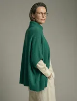 Capa o poncho tejido color verde esmeralda, con cuello polera alto que se cierra con un botón grande en el lateral. Presenta mangas cortas estilo japonesa y un calce amplio.