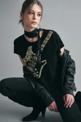 Remera negra de algodón con cuello redondo y mangas cortas. Estampa frontal bordada con lentejuelas doradas y negras formando una guitarra.