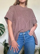 Chaleco tejido color marrón claro, con cuello alto y diseño de trenzas y ochos. Silueta oversize y mangas cortas.