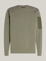 Buzo verde militar de Tommy Hilfiger, de corte clásico con cuello redondo y mangas largas. Presenta un pequeño logo bordado en el pecho y un bolsillo con cremallera en la manga izquierda.