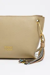 Bolso bandolera de piel vacuna negra, con forma trapezoidal y estructura rígida. Posee asa regulable, cierre de cremallera, bolsillo interior y charm decorativo con borlas en tonos tierra y dorado.