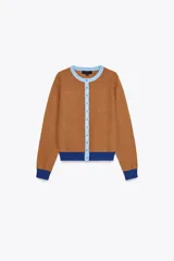 Chaqueta marrón de punto con cuello redondo y manga larga. Presenta cierre frontal con botones y detalles color block en azul en cuello, puños y ruedo.