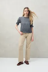 Blusa azul grisáceo de algodón con bordados frontales y terminaciones festoneadas. Tiene mangas cortas con frunces y cuello redondo con detalle de puntilla.