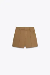 Shorts color marrón claro confeccionados en hilatura con algodón, de tiro alto y doble cintura con trabillas. Presentan bolsillos laterales, falso bolsillo con solapa en delantero y costuras a contraste.