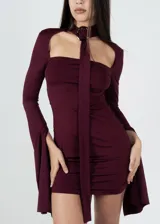 Vestido corto color borgoña, ajustado al cuerpo, con escote recto, mangas largas acampanadas y gargantilla con hebilla plateada.
